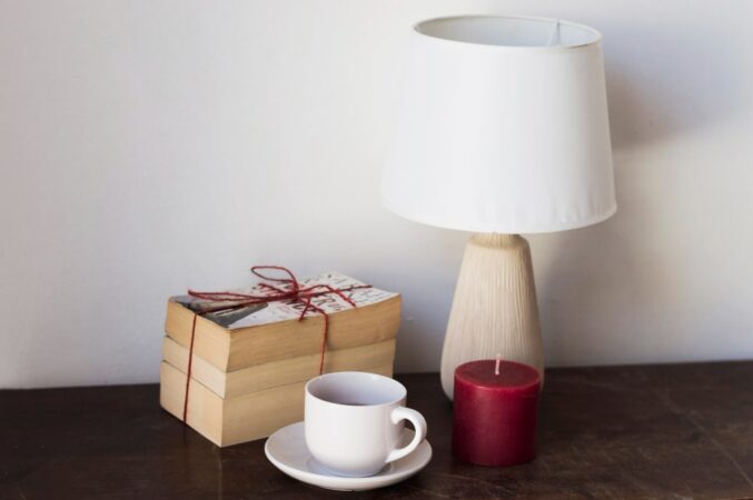 Élégante lampe de chevet en bois avec abat-jour blanc, posée sur une table sombre à côté d'une tasse de café et de livres reliés